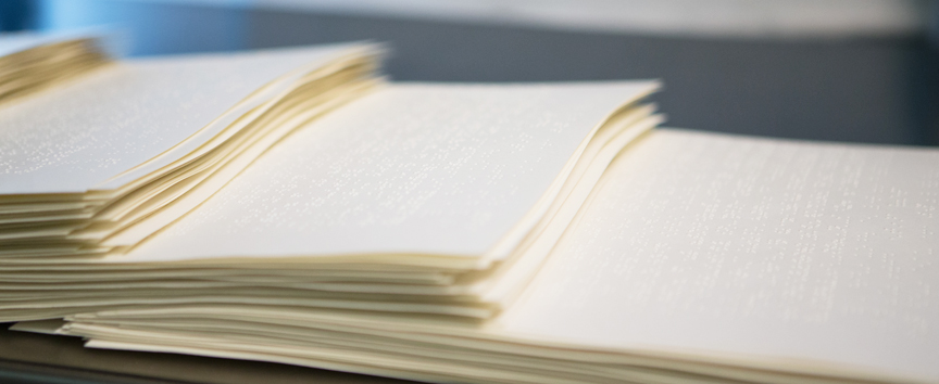 Close-up image of 3 stacks of braille papers laid out on a table.