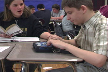 Photo of a teenaged boy using a braille PDA in class.