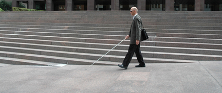 Photo of Chris walking, with cane, through some complicated outdoor staircases in a plaza