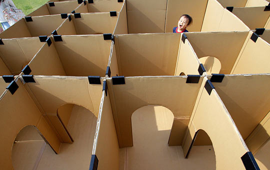 Kid's head pops up in the middle of a large cardboard maze