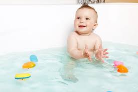 baby sits in a bath tub with bath toys