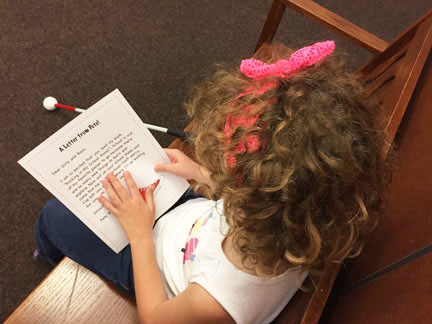 Girl reads the print/braille letter from Pete.