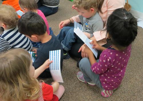 Group of kids sit on the floor, holding and examining braille alphabet cards.